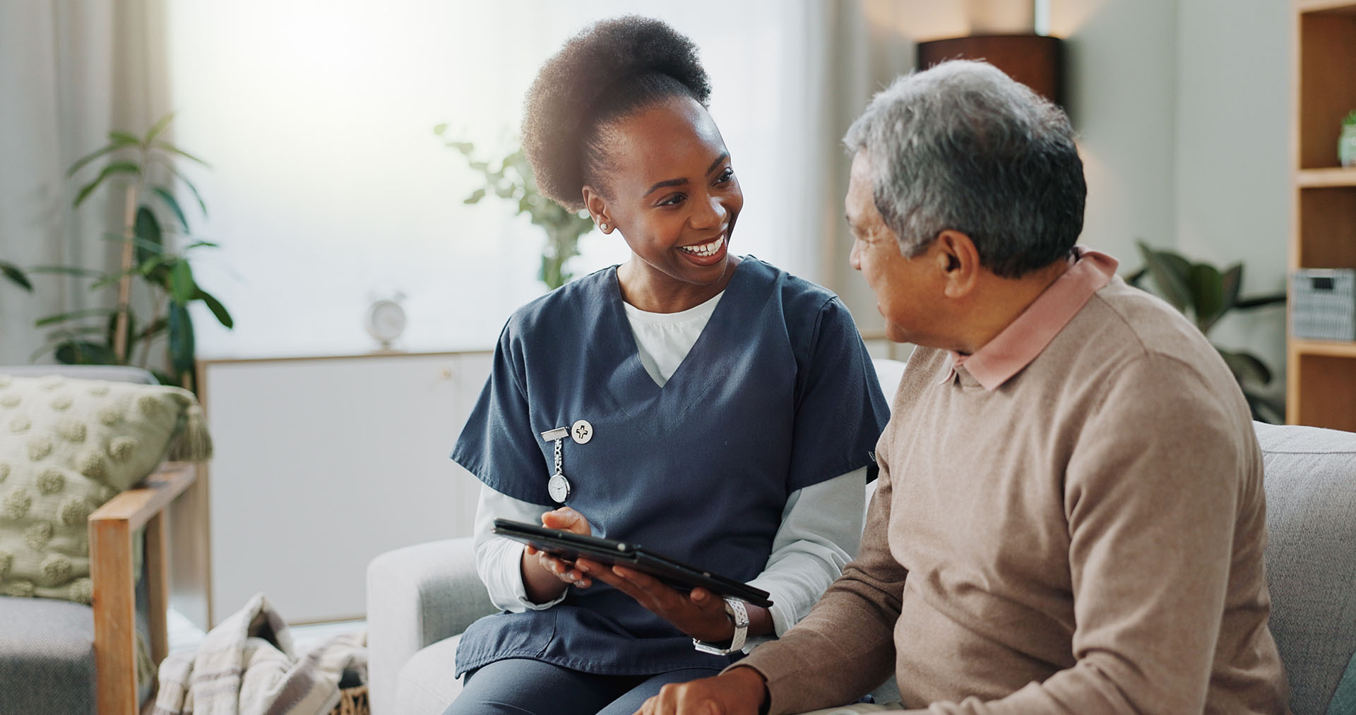 Tablet, healthcare and nurse in home with senior man, internet and online help on sofa. Young caregiver, elderly person and technology for learning or telehealth and care in chronic illness
