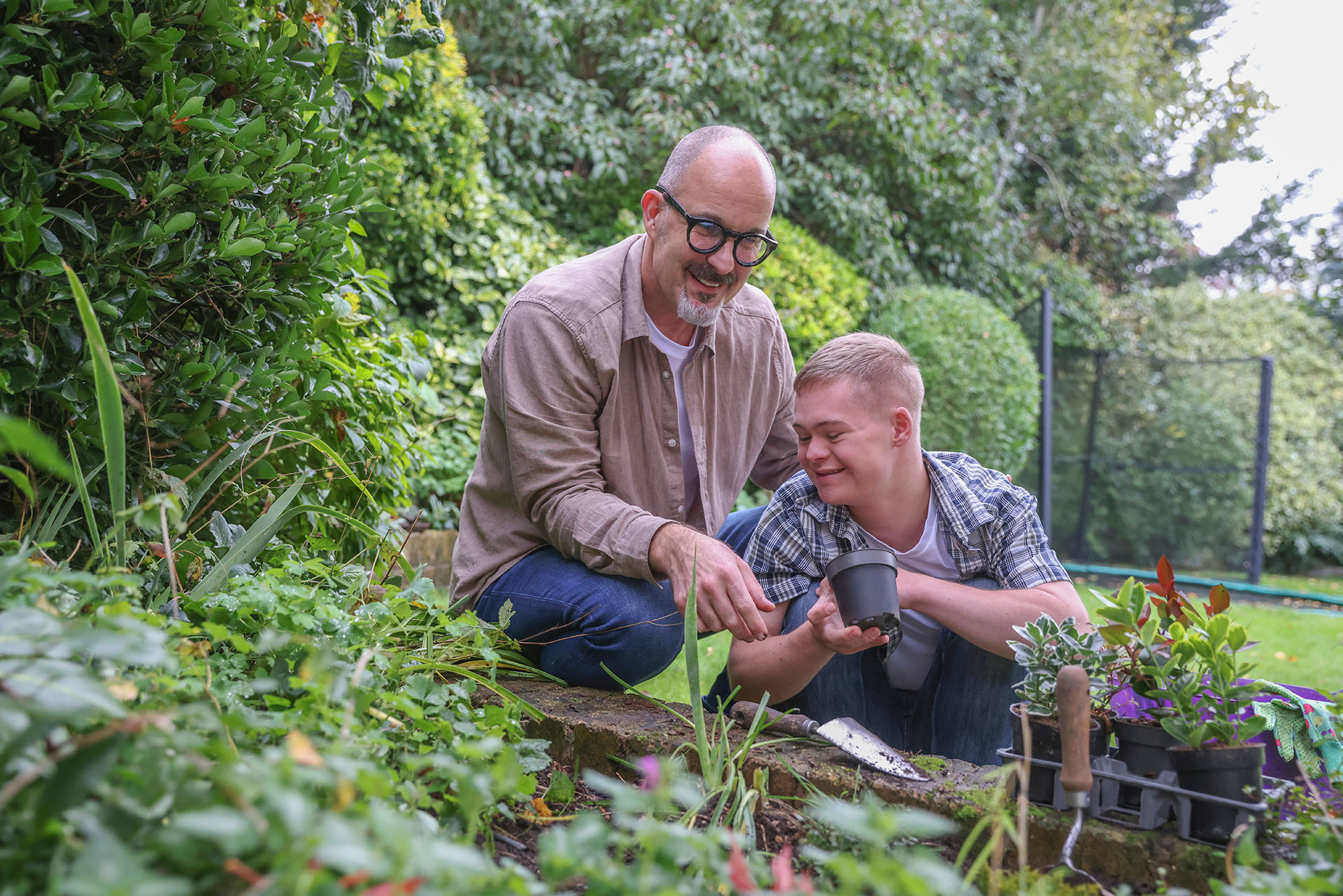 Mature father with adult son planting in garden